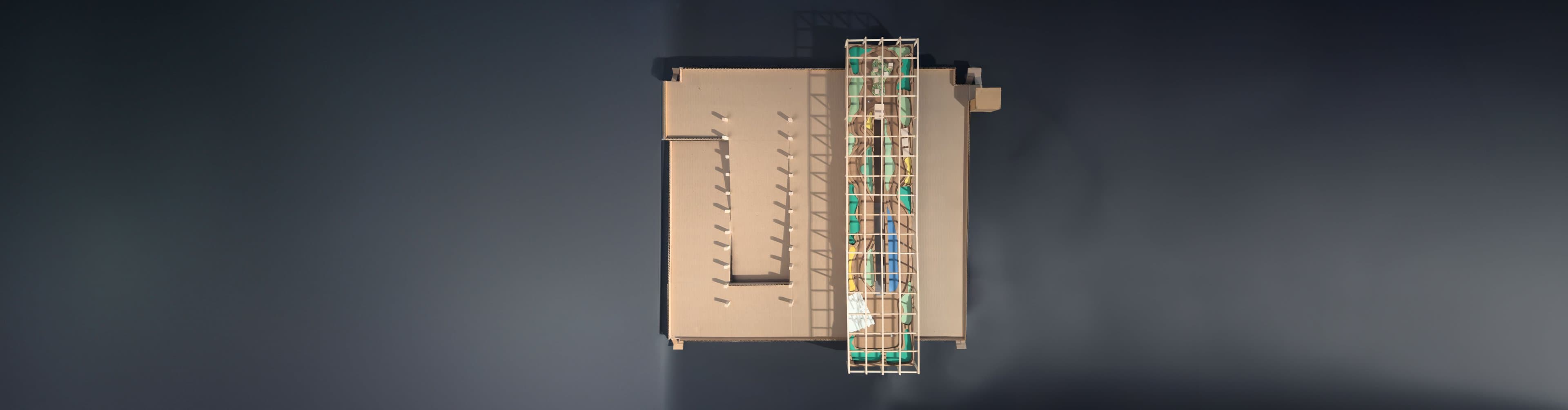 Overhead photo of the SkyFarm model: a cardboard parking structure topped by a long timber-grid rooftop farm.