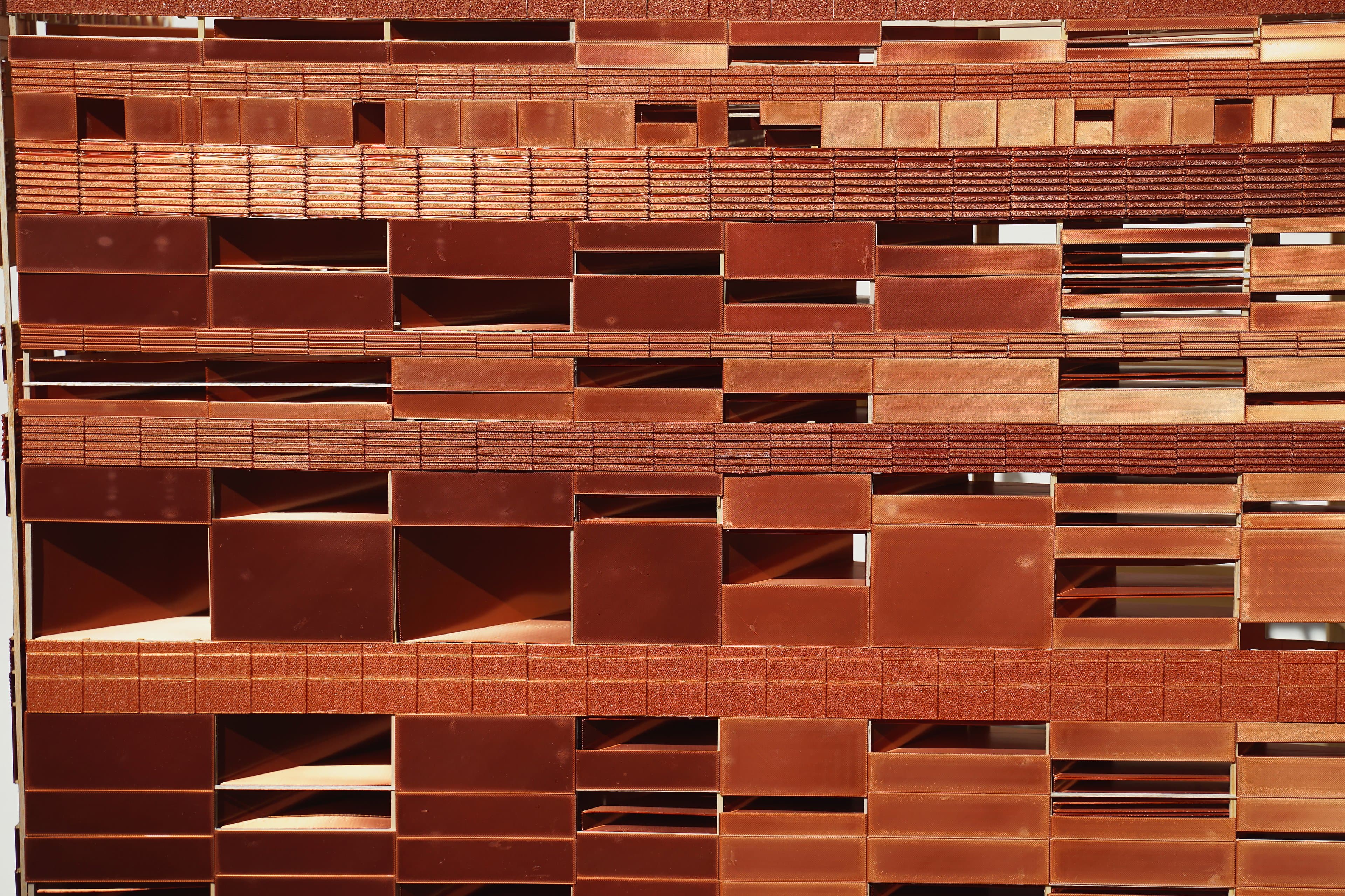 Close-up of the Strata model's copper rainscreen: rows of solid, perforated and corrugated panels with deep openings, in raking sun.